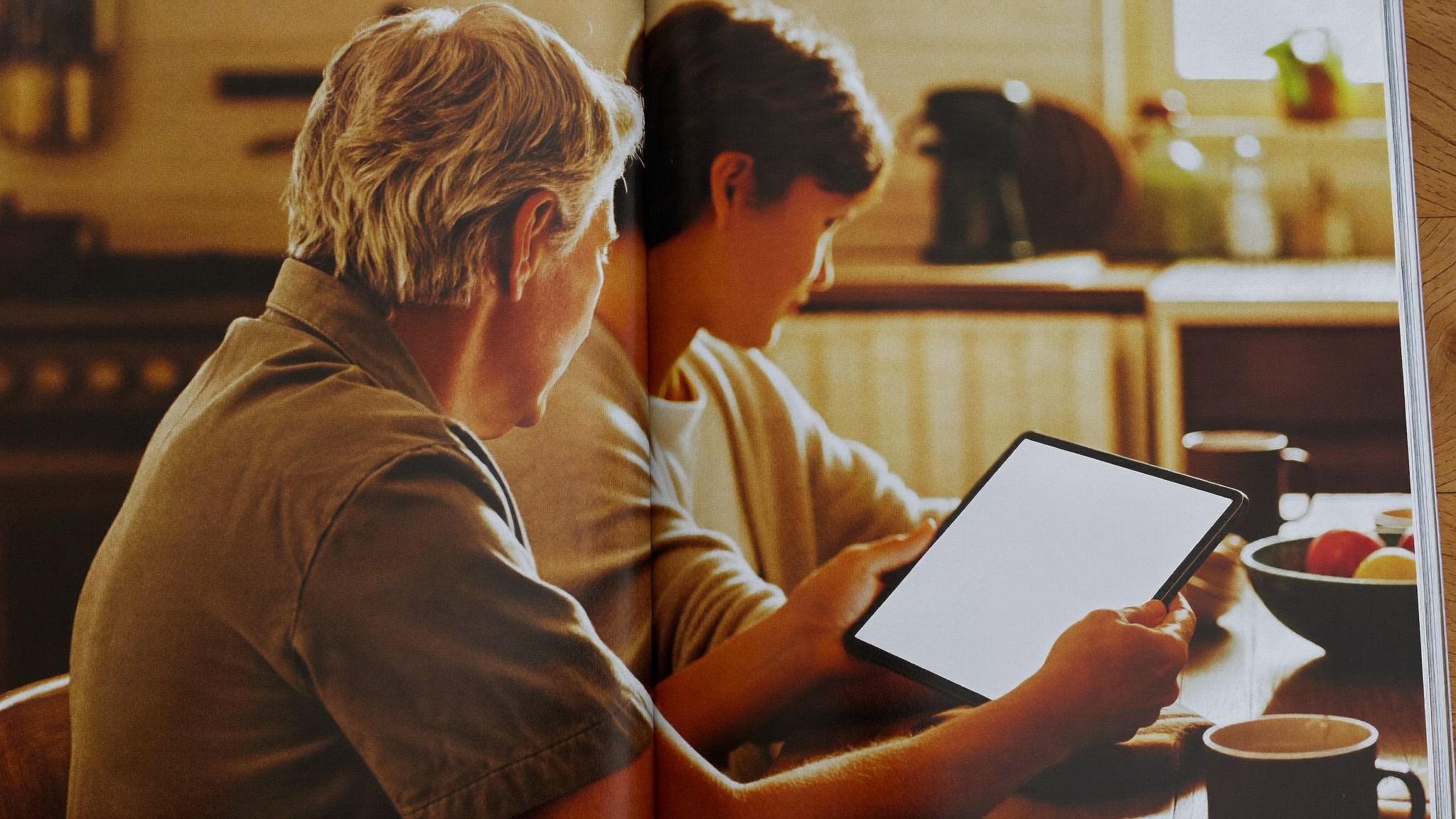A multigenerational family gathered around a dining table, an older parent and adult child reviewing account settings together on a tablet